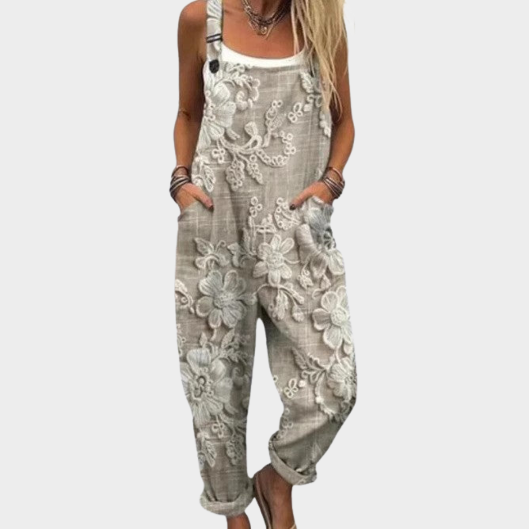 Woman wearing beige-grey dungarees with a subtle tone-on-tone floral print, adjustable straps, elegant and relaxed.