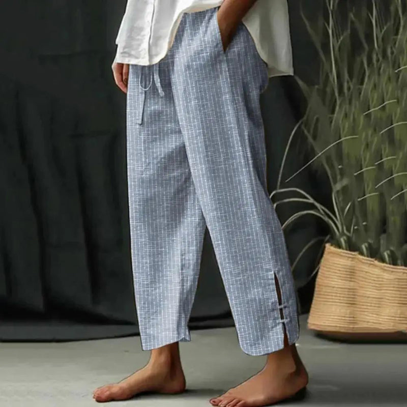 Woman wearing tapered drawcord-waist trousers with sandals, standing in a sunlit garden.