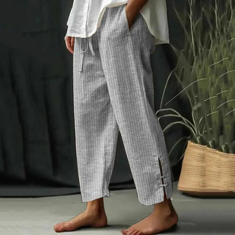 Woman wearing tapered drawcord-waist trousers with sandals, standing in a sunlit garden.