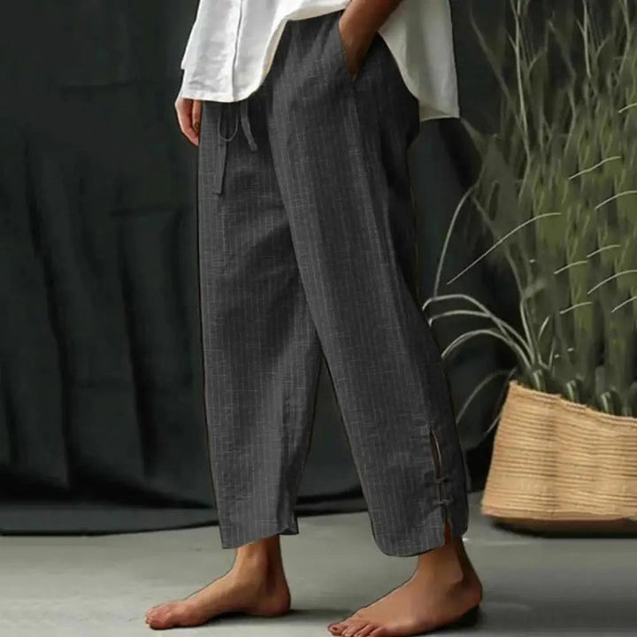 Woman wearing tapered drawcord-waist trousers with sandals, standing in a sunlit garden.
