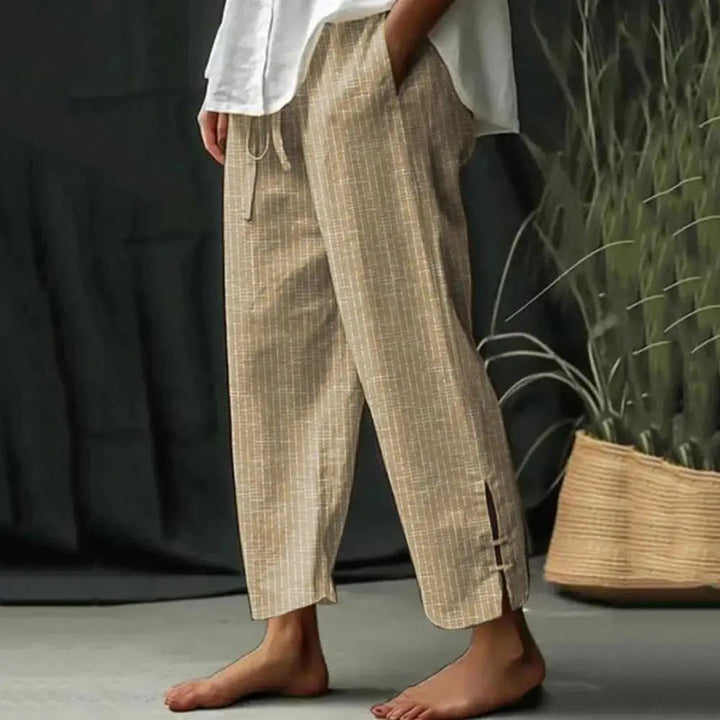 Woman wearing tapered drawcord-waist trousers with sandals, standing in a sunlit garden.