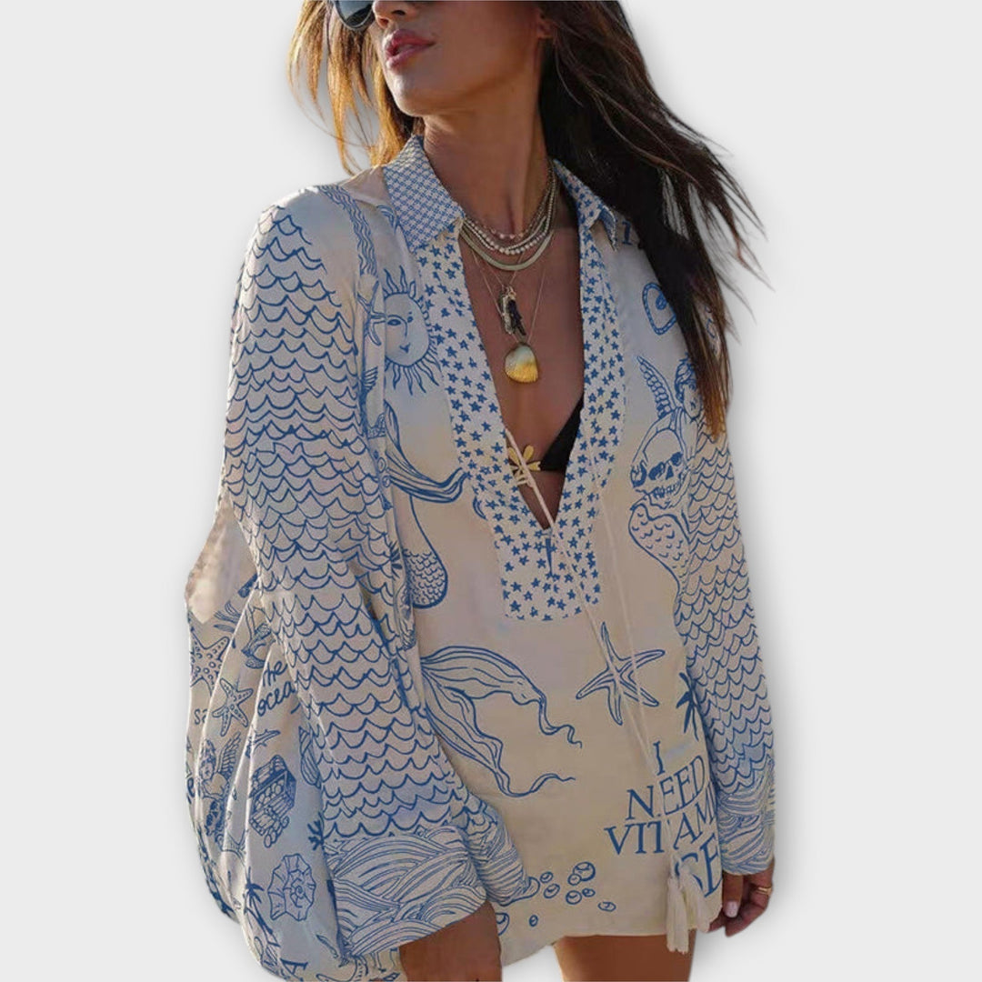 Woman walking on the beach in a relaxed tunic dress with playful maritime print and tie collar.