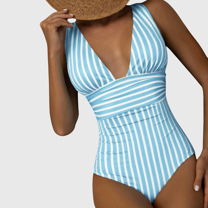 A woman walking by the sea in a bright printed swimsuit, relaxed and glowing in the sun.
