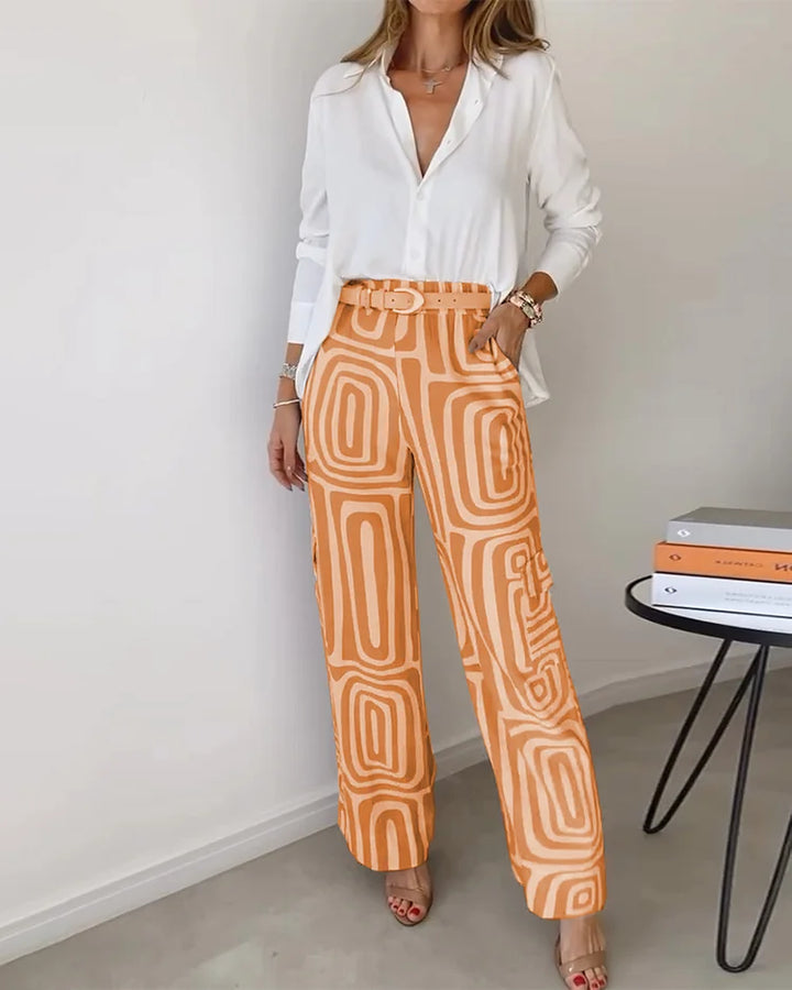 A woman wearing a plain button-up top with geometric-print trousers and a belt at the waist.
