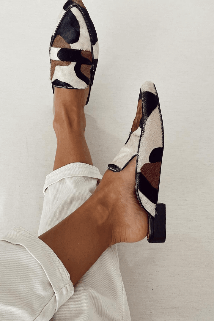 A woman wearing pointed cow-print loafers in warm brown, black and cream