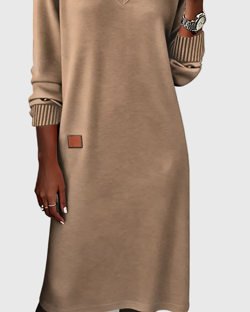 Woman wearing the Emma flowing elegant dress in beige, standing relaxed and smiling.