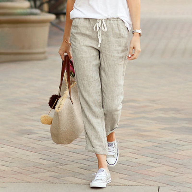 Woman wearing flared drawcord-waist trousers with trainers, walking through town.