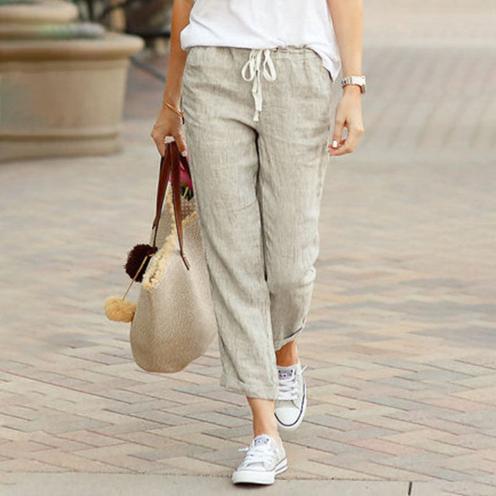 Woman wearing flared drawcord-waist trousers with trainers, walking through town.
