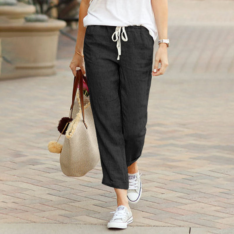 Woman wearing flared drawcord-waist trousers with trainers, walking through town.