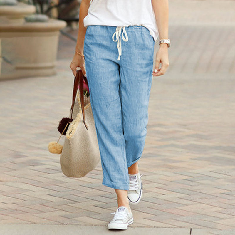 Woman wearing flared drawcord-waist trousers with trainers, walking through town.