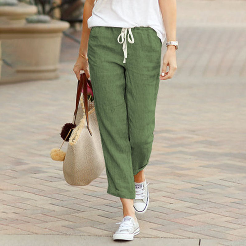 Woman wearing flared drawcord-waist trousers with trainers, walking through town.