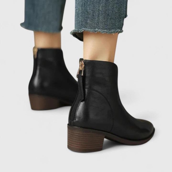 Woman wearing black elegant boots with tailored trousers on a city footpath.