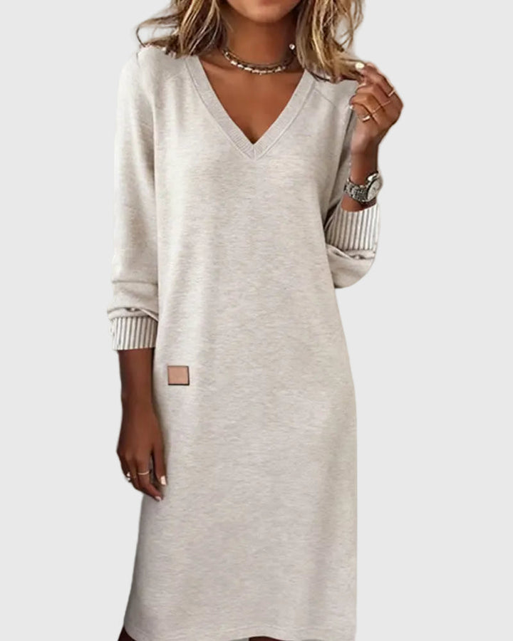 Woman wearing the Emma flowing elegant dress in beige, standing relaxed and smiling.