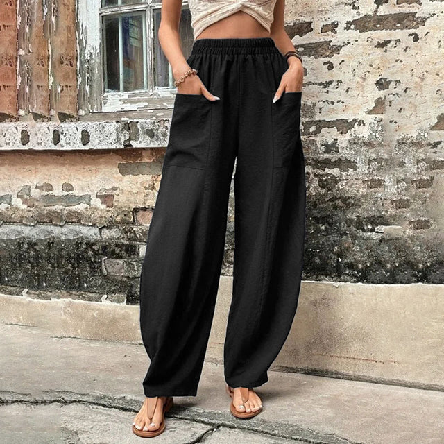 A woman walking in flowing wide-leg trousers with big patch pockets and an elegant, draped silhouette.