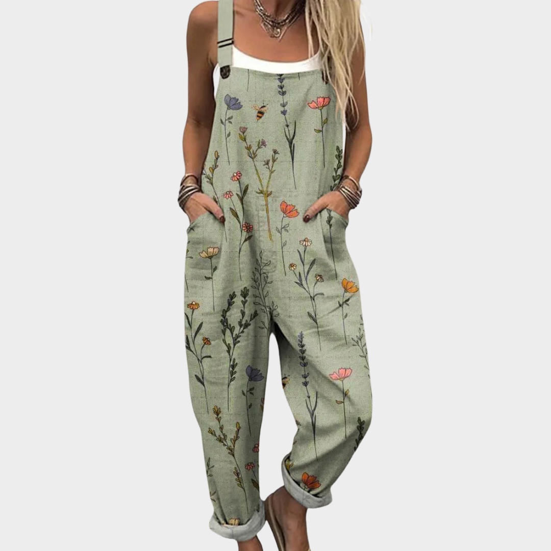 A woman wearing soft sage green dungarees scattered with delicate wildflowers, with adjustable straps.