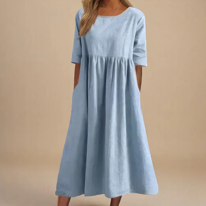 A woman wearing the Carmel flowing day dress with a gathered waist and elbow-length sleeves.
