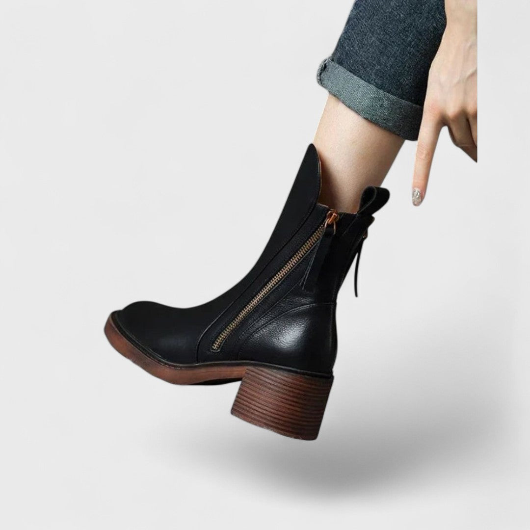 Woman wearing black refined ankle boots with tailored trousers in a city setting.