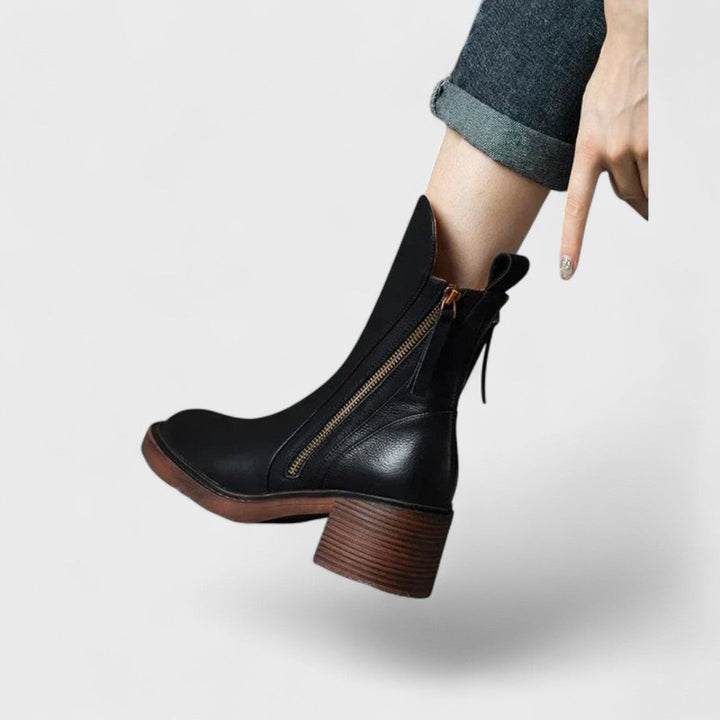 Woman wearing black refined ankle boots with tailored trousers in a city setting.