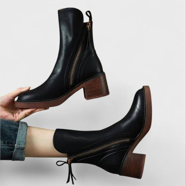 Woman wearing black refined ankle boots with tailored trousers in a city setting.