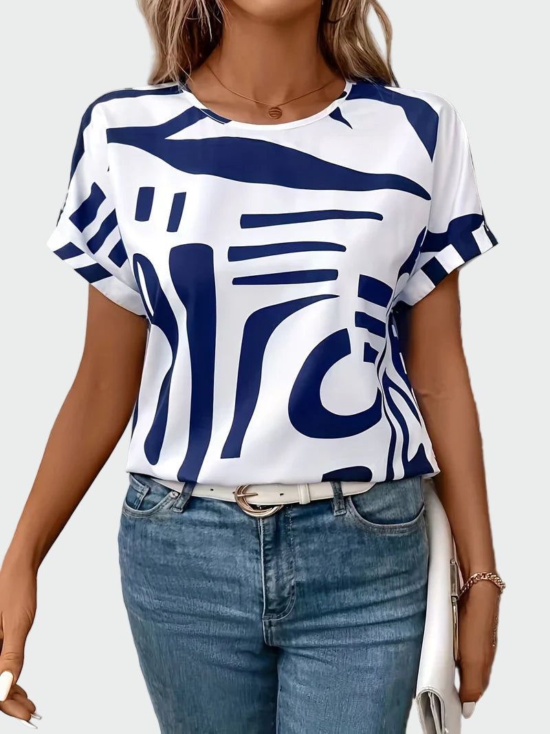 Women's white short-sleeve blouse with a bold blue abstract geometric print and rolled sleeve hems