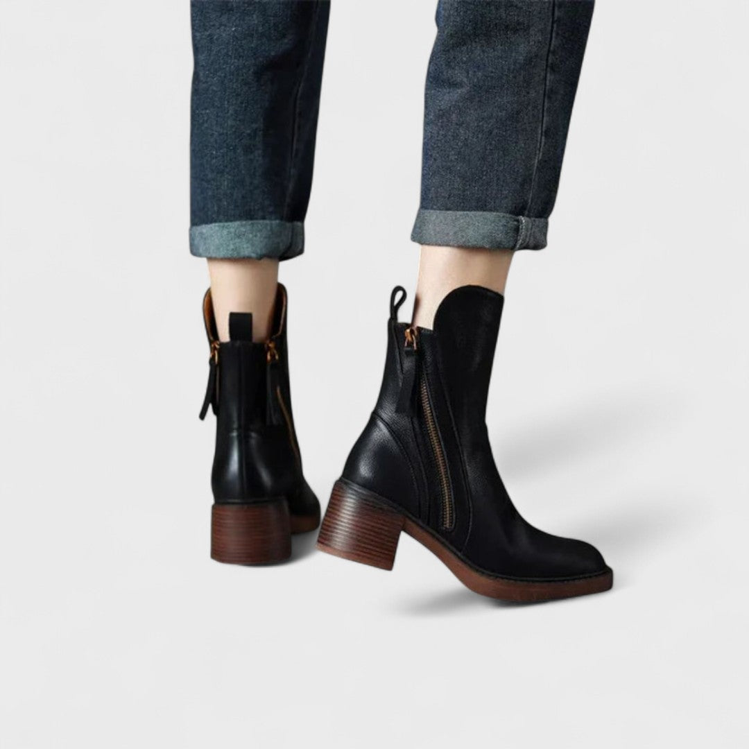 Woman wearing black refined ankle boots with tailored trousers in a city setting.