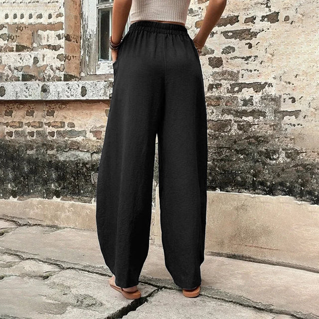 A woman walking in flowing wide-leg trousers with big patch pockets and an elegant, draped silhouette.