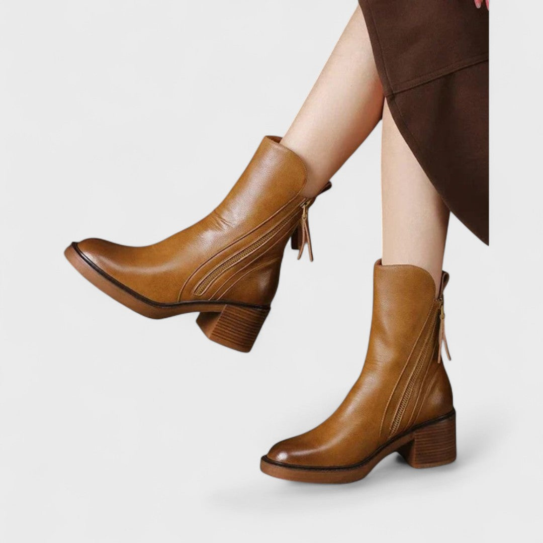 Woman wearing black refined ankle boots with tailored trousers in a city setting.