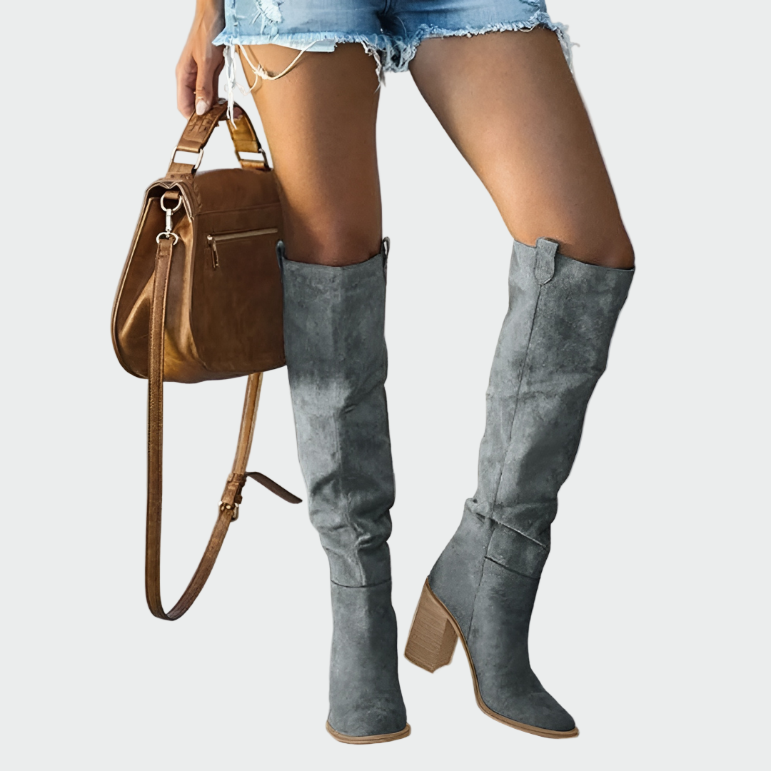 A woman in a dress wearing warm brown Western-style ankle boots with a sturdy heel.