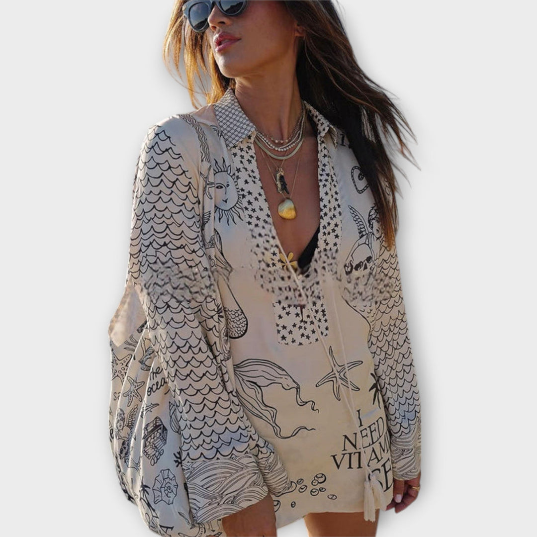 Woman walking on the beach in a relaxed tunic dress with playful maritime print and tie collar.