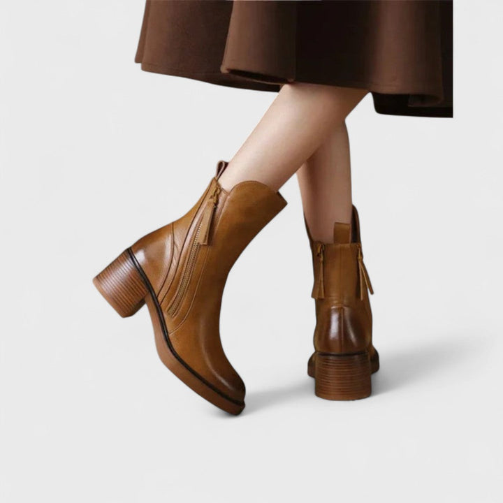 Woman wearing black refined ankle boots with tailored trousers in a city setting.