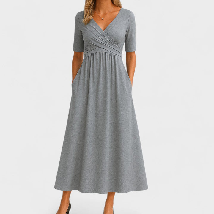 Woman wearing a mid-calf dress with a crossover V-neckline, gathered waist and gently flared skirt.