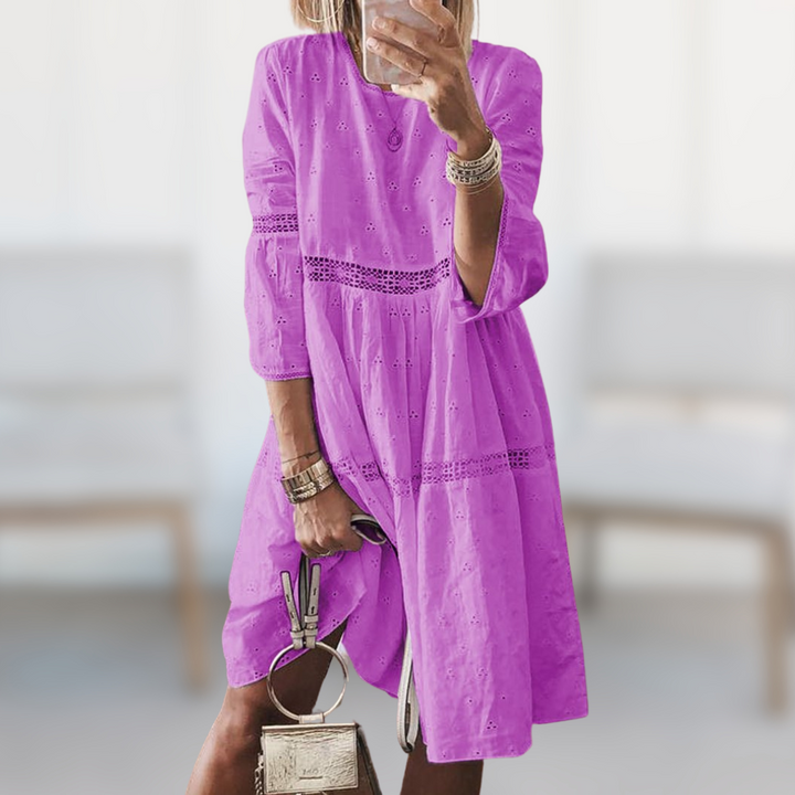 Woman wearing the Majella™ elegant summer dress with a round neckline and flowing silhouette, standing outdoors on a sunny day.