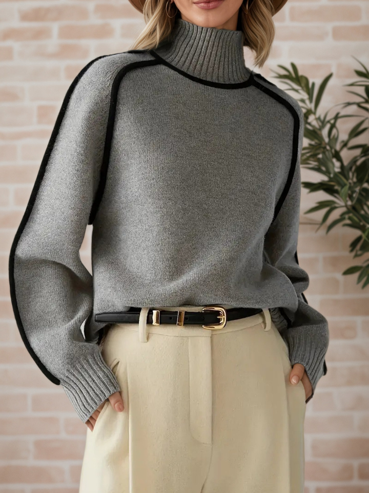 A woman wearing a funnel neck jumper with contrast piping, styled with trousers for a smart-casual look.