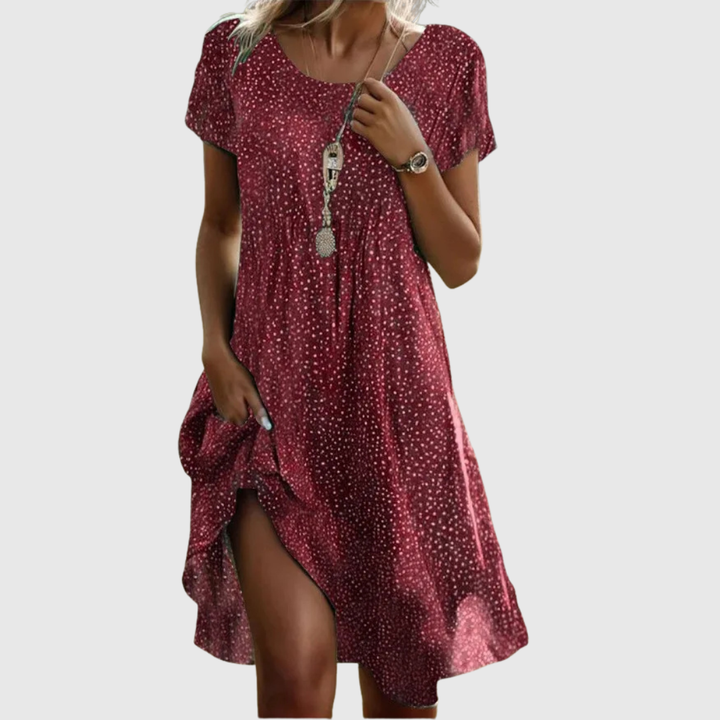 Woman wearing the Amy speckled summer dress in green, smiling in the sunshine outdoors.