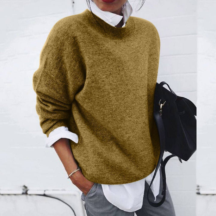 A woman wearing a soft mustard round-neck jumper with an elegant modern shape, relaxed and warm.