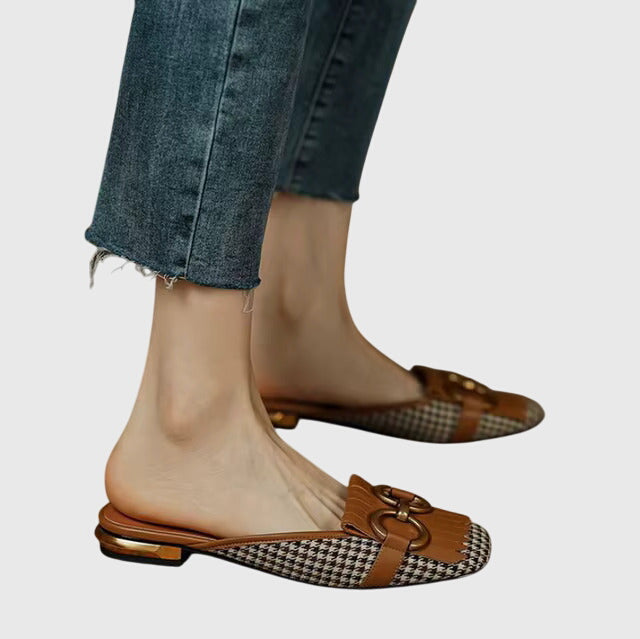 A cream closed-toe mule with a gold horsebit ring detail and a low heel.