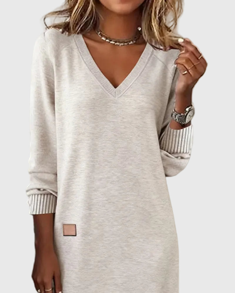 Woman wearing the Emma flowing elegant dress in beige, standing relaxed and smiling.