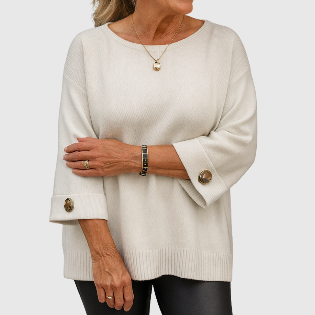 A woman wearing a cream jumper with a wide round neck and gold-toned buttons on the cuffs.