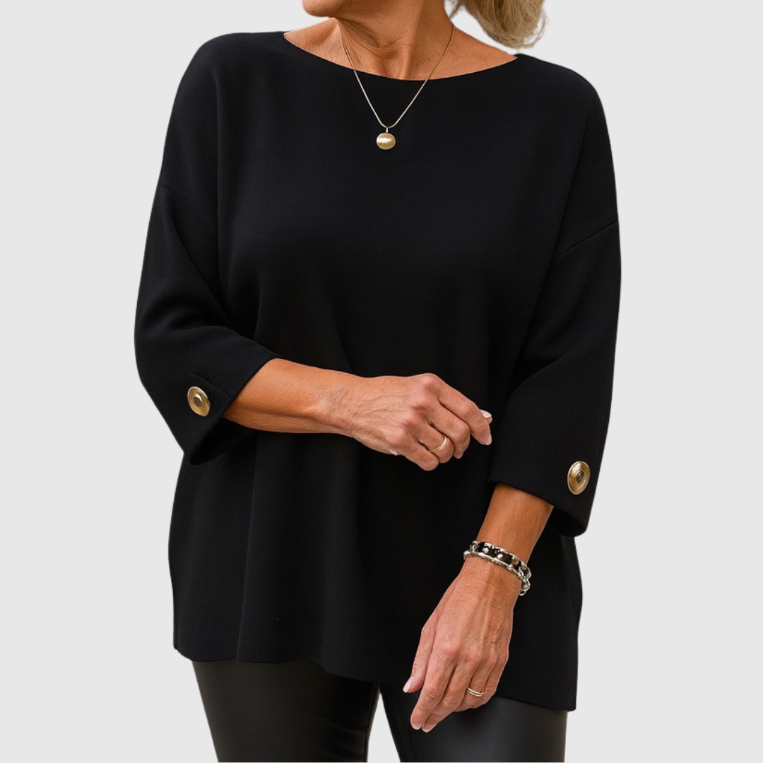 A woman wearing a cream jumper with a wide round neck and gold-toned buttons on the cuffs.