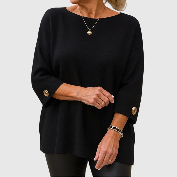 A woman wearing a cream jumper with a wide round neck and gold-toned buttons on the cuffs.