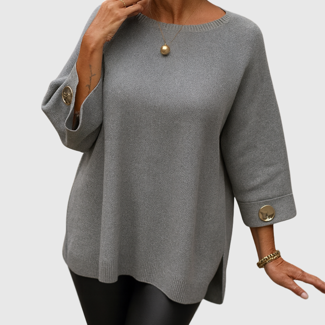 A woman wearing a cream jumper with a wide round neck and gold-toned buttons on the cuffs.