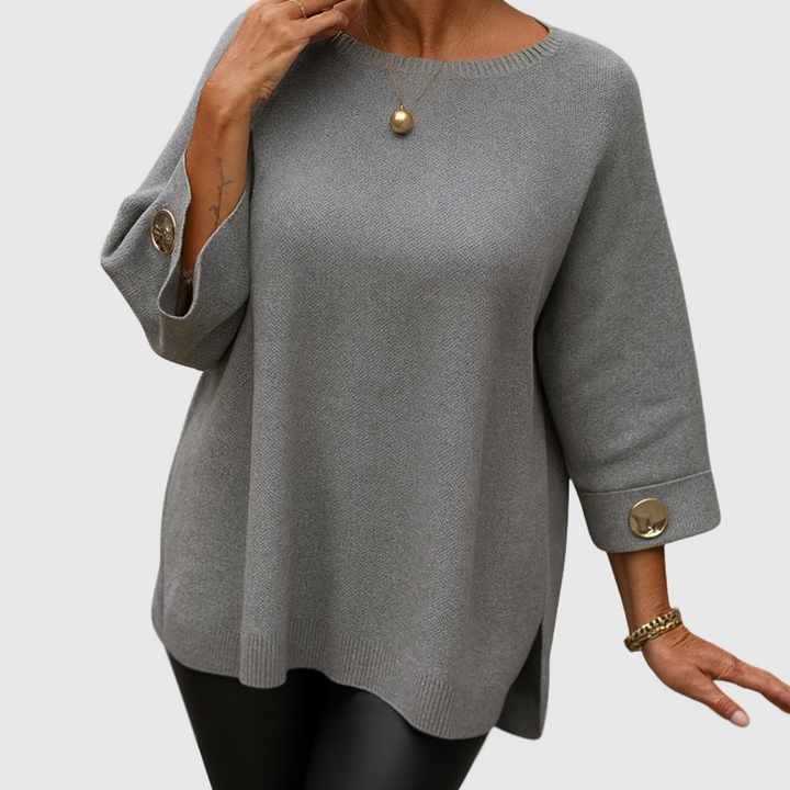 A woman wearing a cream jumper with a wide round neck and gold-toned buttons on the cuffs.