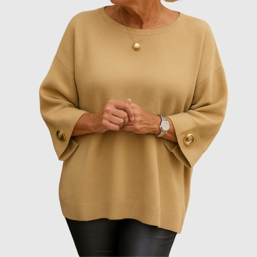 A woman wearing a cream jumper with a wide round neck and gold-toned buttons on the cuffs.