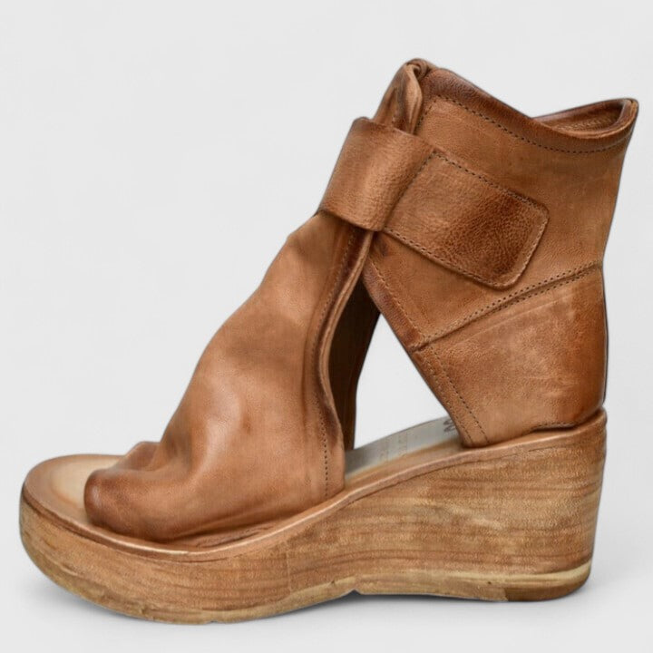 A woman in tan buckle wedge sandals, walking easily on a summer afternoon.