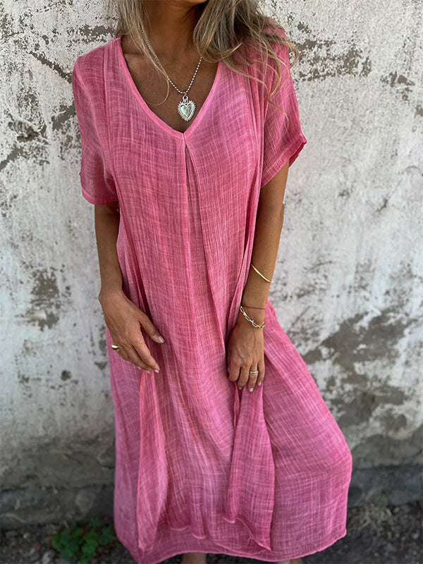 Woman wearing the Dolores™ flowing V-neck dress with short sleeves, standing relaxed in warm sunlight.