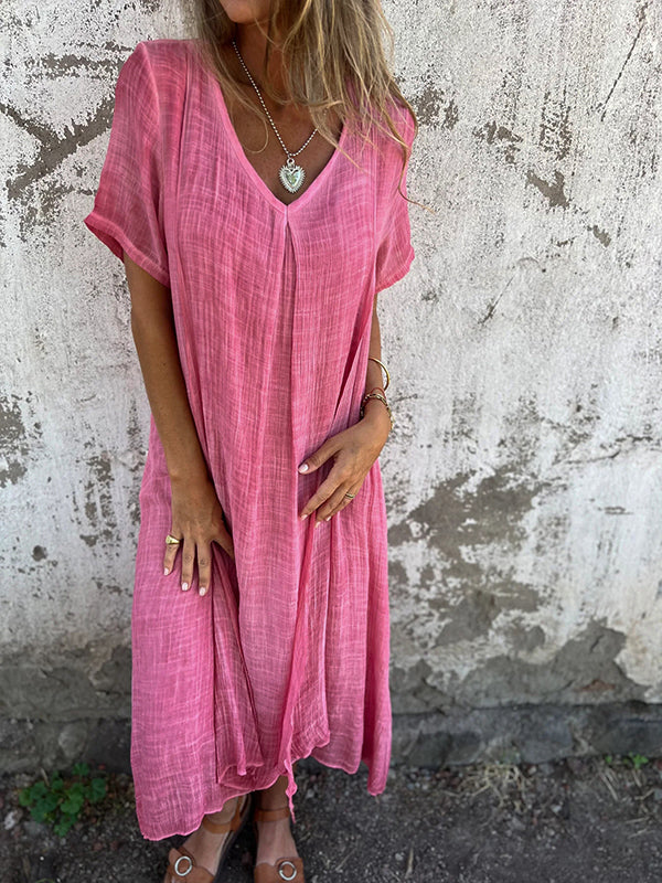 Woman wearing the Dolores™ flowing V-neck dress with short sleeves, standing relaxed in warm sunlight.