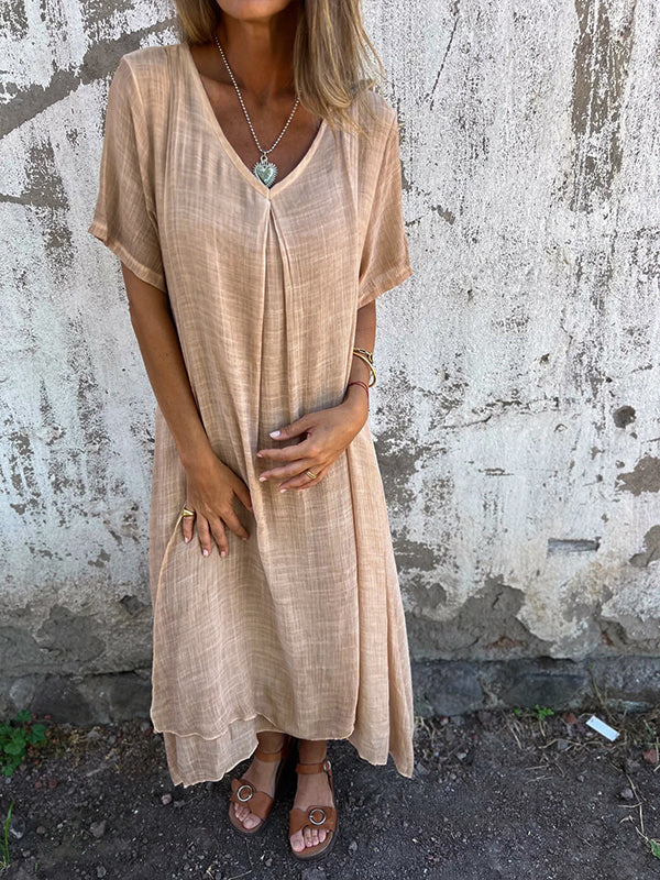 Woman wearing the Dolores™ flowing V-neck dress with short sleeves, standing relaxed in warm sunlight.