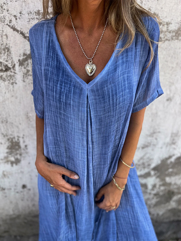 Woman wearing the Dolores™ flowing V-neck dress with short sleeves, standing relaxed in warm sunlight.