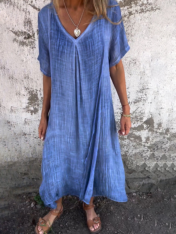 Woman wearing the Dolores™ flowing V-neck dress with short sleeves, standing relaxed in warm sunlight.