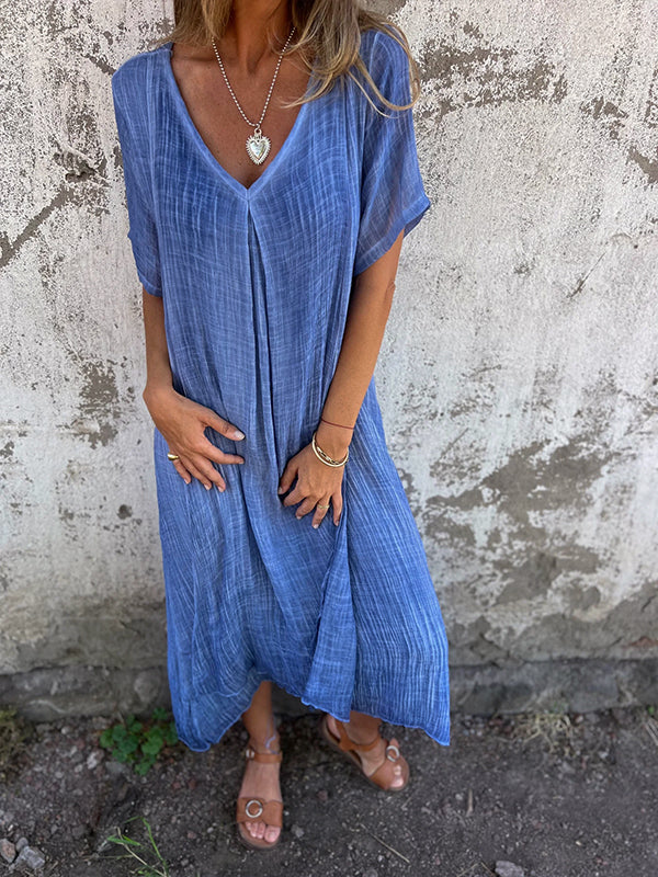 Woman wearing the Dolores™ flowing V-neck dress with short sleeves, standing relaxed in warm sunlight.